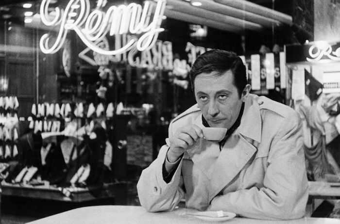 Sieben Tote hat die Woche: Jabeke (Jean Rochefort), in einen Trenchcoat gekleidet, beobachtet beim Kaffeetrinken die Szenerie. Bild: Sender /&copy; 1963 Warner Bros. / Entertainment France / Pathe Films / Dear Film / Ultra Film