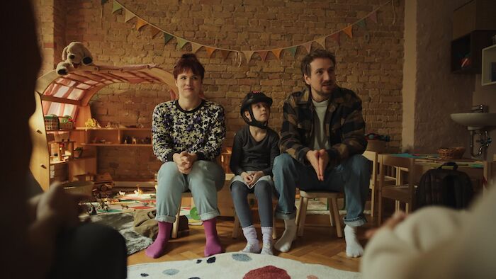 Fang mich doch! Die Eltern Mara Sommer (Pina Bergemann) und Georg Sommer (Jan Krauter) sitzen mit ihrer Tochter Bernadette (Elise Lindner) in der Kita Regenbogen und stellen sich den Kitaeltern vor. Bild: Sender / ZDF / Omri Alon